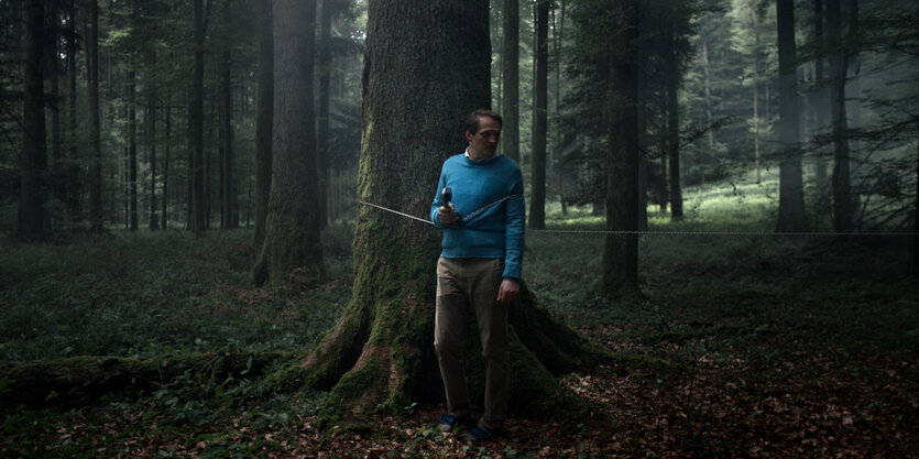 Im dunklen Wald steht ein Mann mit Telefonhörer.