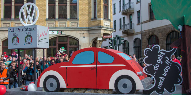 Ein Karenvalswagen mit dem Motiv als roter VW-Käfer stößt eine Abgaswolke aus, auf der „Da geht noch was!!!“ steht.
