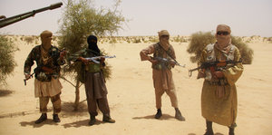 Vier bewaffnete und maskierte Männer in der Wüste.