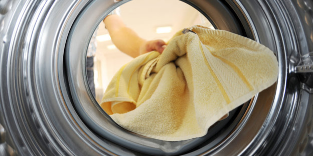 Eine Hand steckt ein Handtuch in eine Waschmaschine hinein