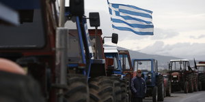 Zahlreiche Traktoren stehen hintereinander auf einer Straße, an einem weht die griechische Fahne.